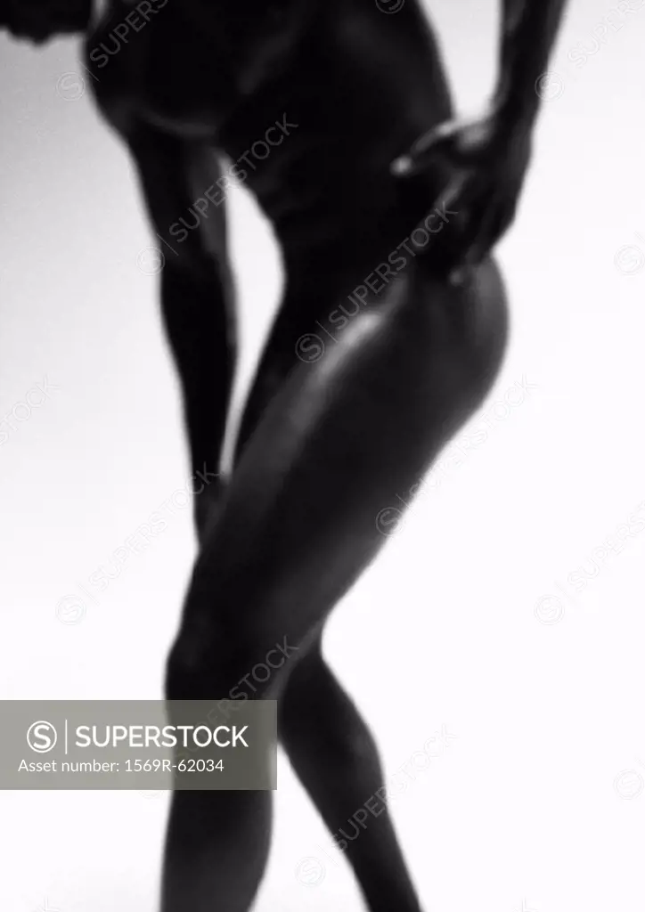 Man standing, bending over and touching hip and knee, black and white