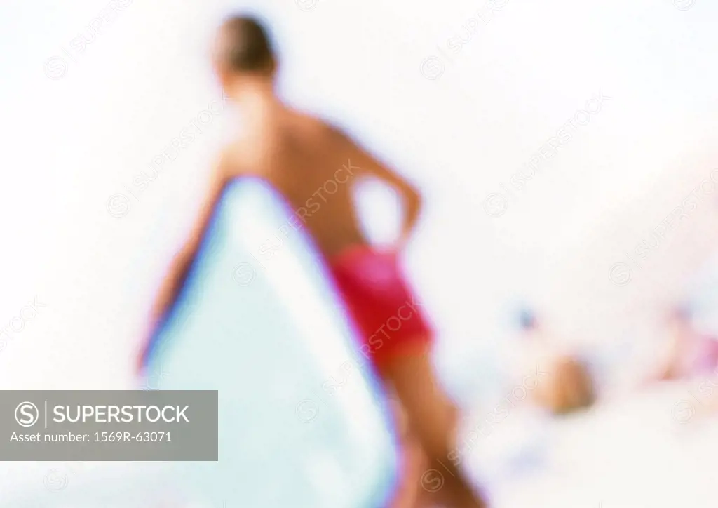 Boy holding boogie board on beach, blurred
