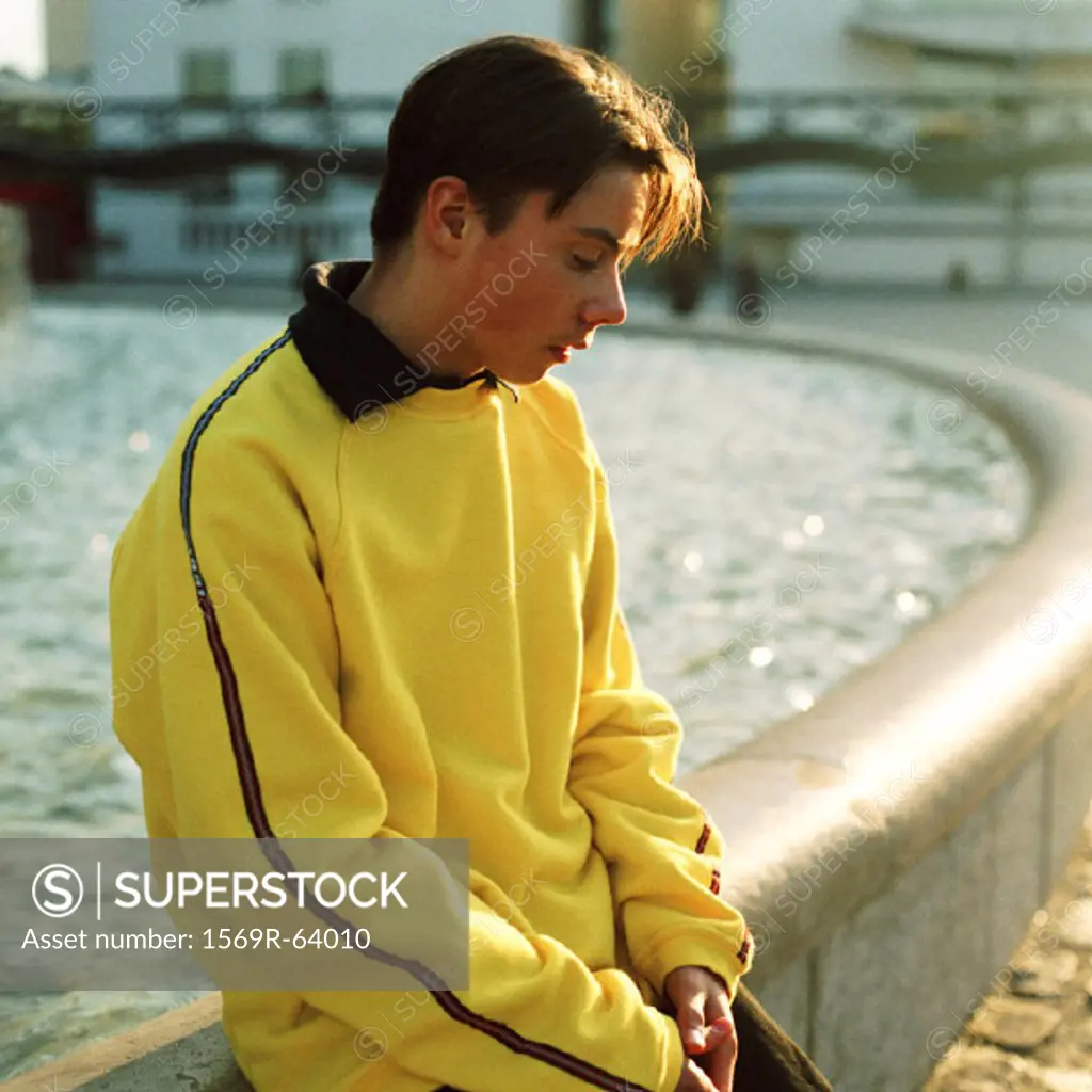 Teenage boy sitting on edge of fountain, looking down