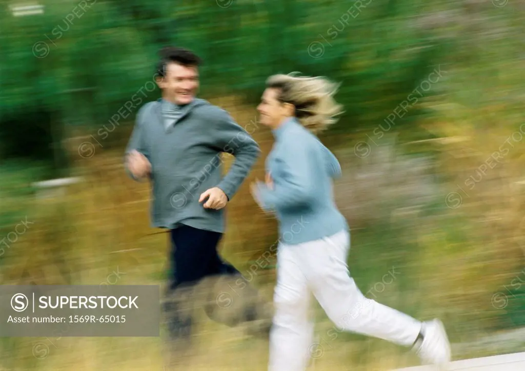 Man and woman jogging together in field, blurred