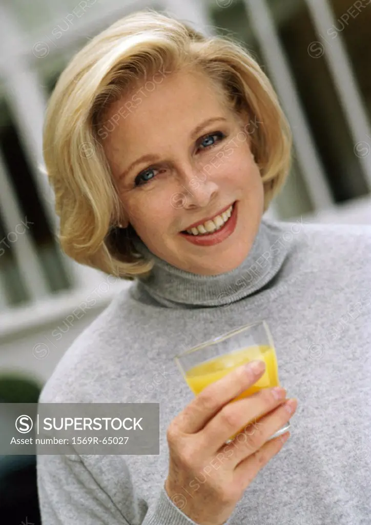 Woman looking at camera holding glass of orange juice, close up, portrait