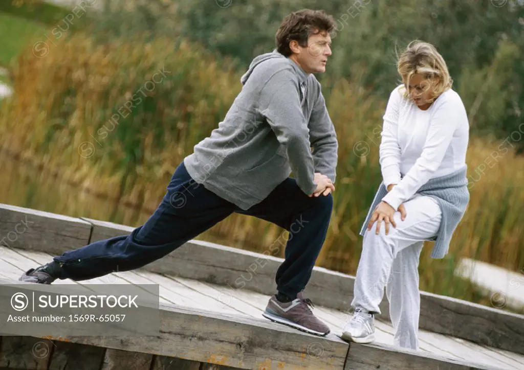 Man and woman stretching legs together on wooden walkway