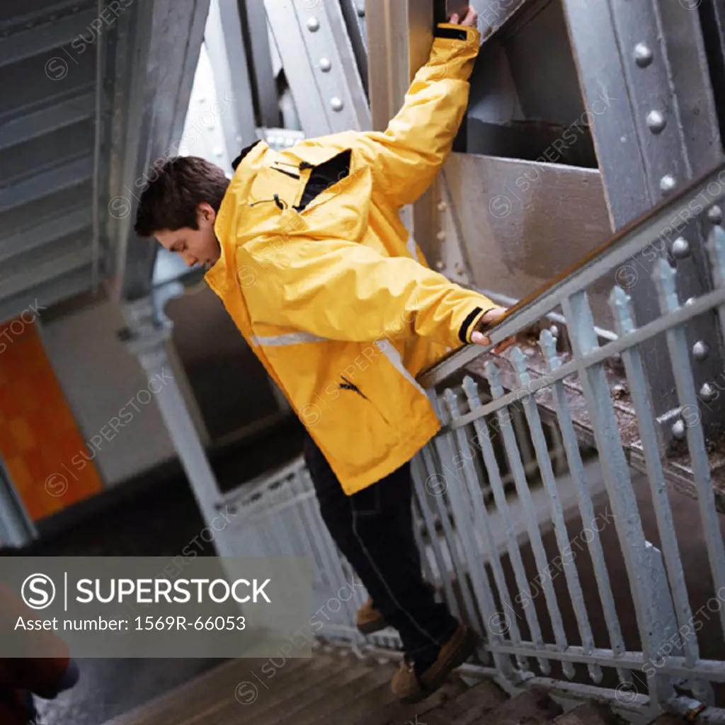 Teenage boy in raincoat sliding down handrail in stairway