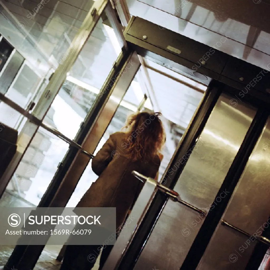 Young woman walking through subway station doorway, view from rear