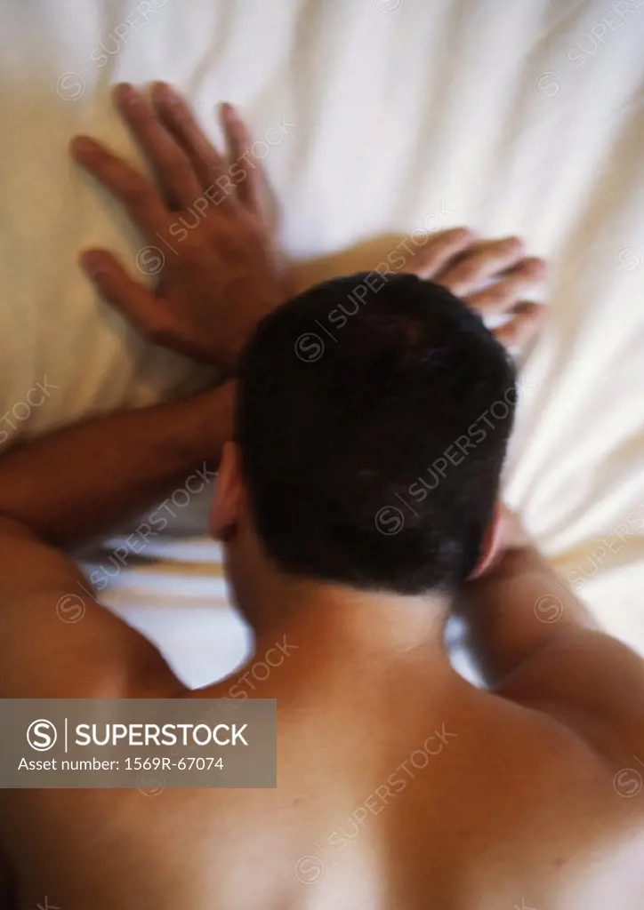 Man lying face down on bed with head on hands, blurred, high angle view