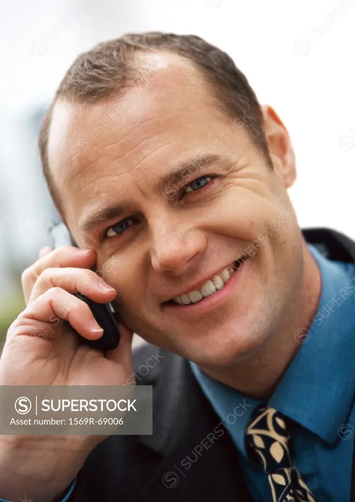 Businessman using cellular phone, smiling at camera, portrait, close-up