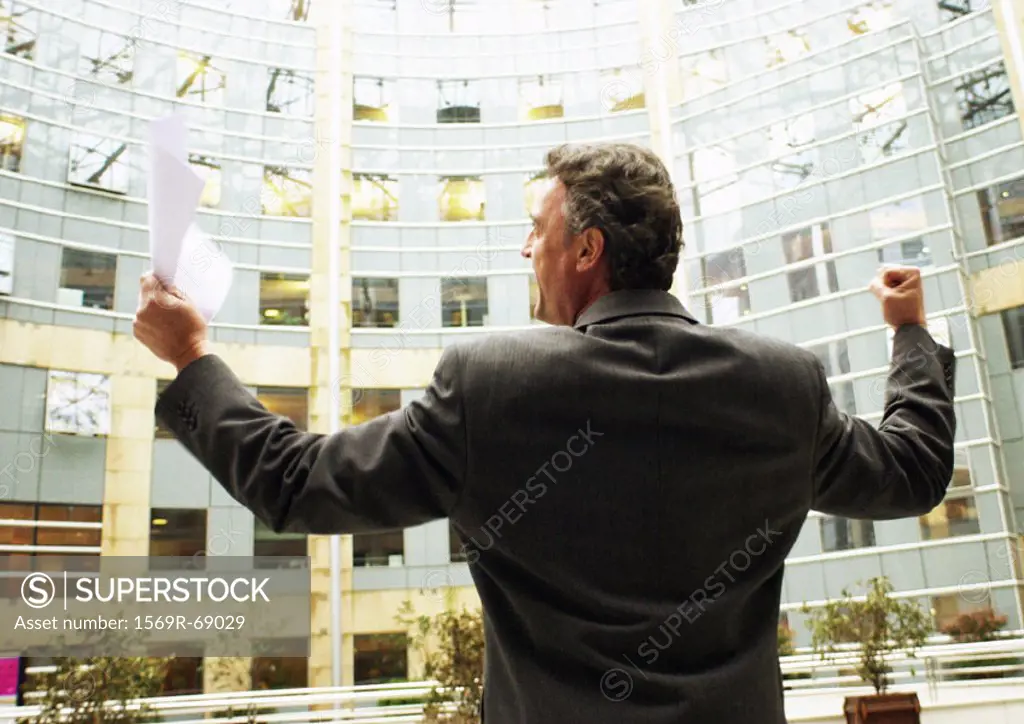 Businessman standing in front of building, arms raised in victorious gesture, rear view