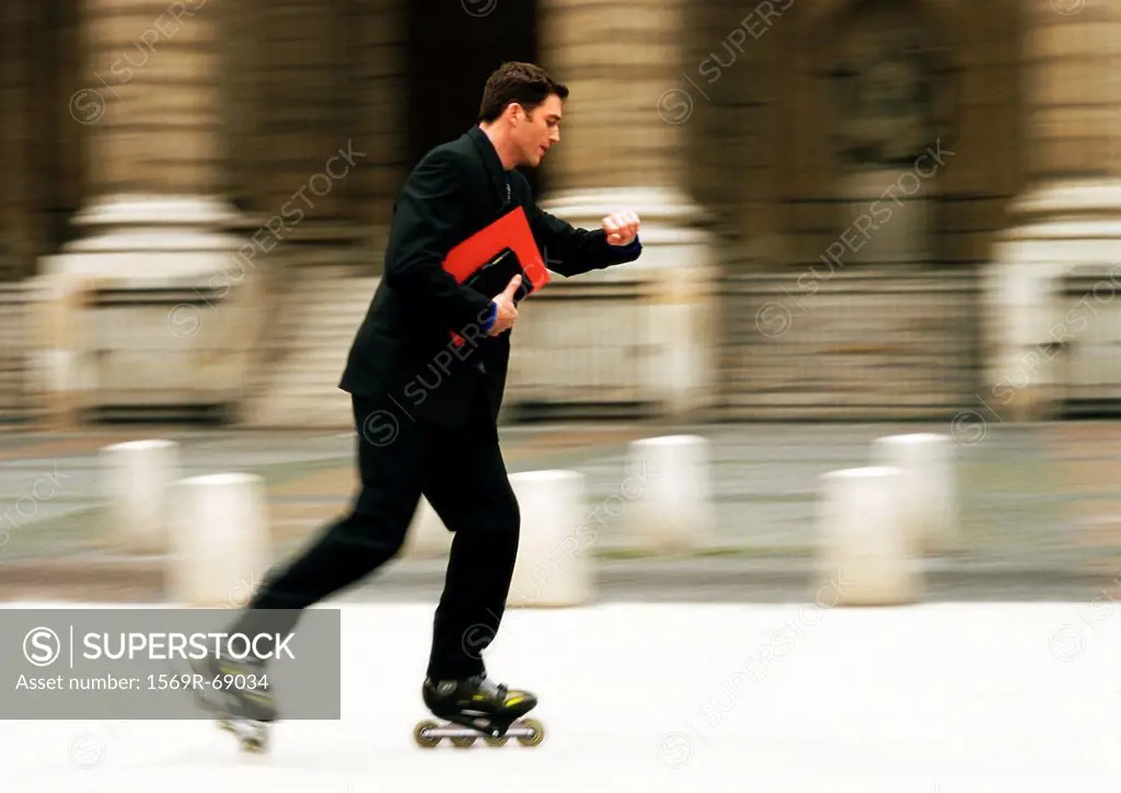 Businessman rollerblading in front of building and checking time, blurred