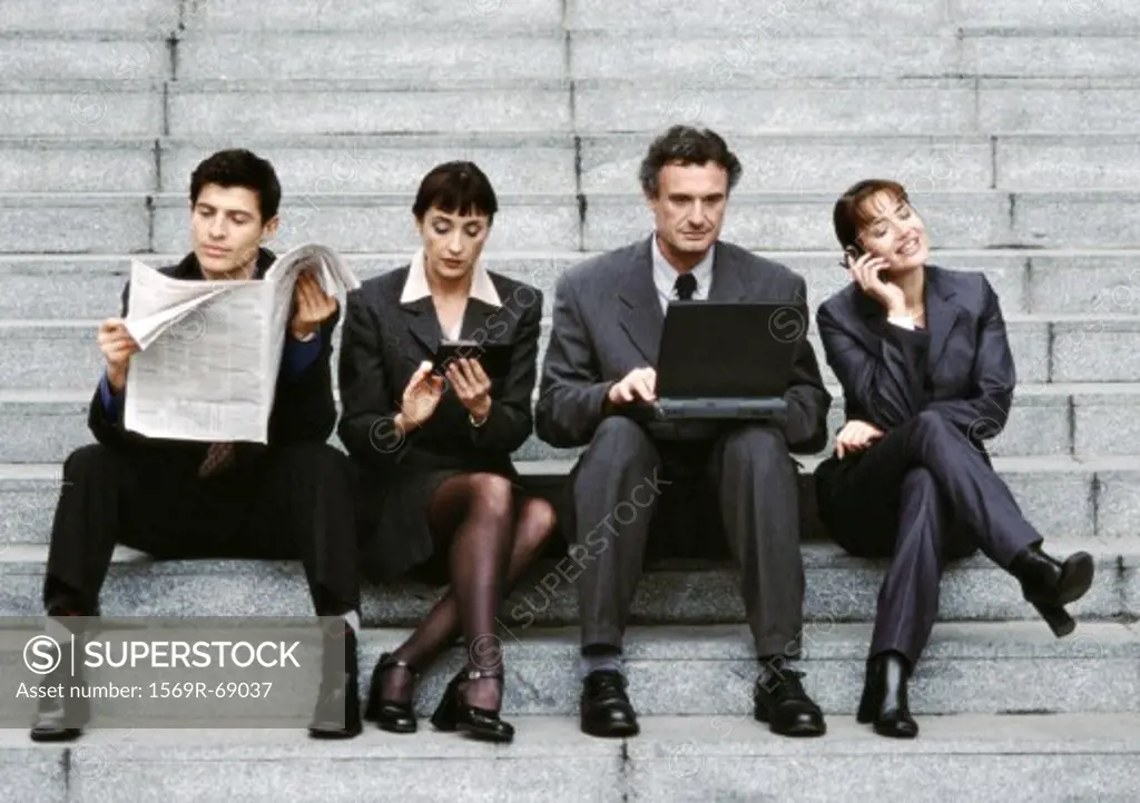 Four business people wearing suits, sitting on steps, reading newspaper