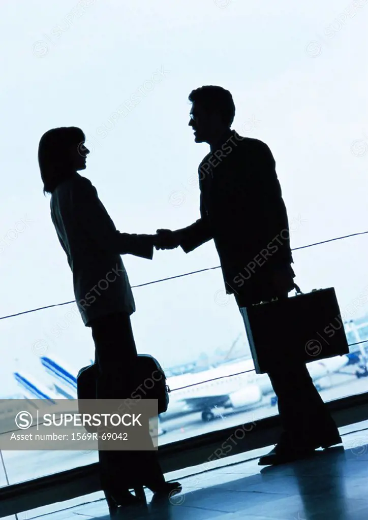 Businessman and businesswoman shaking hands in airport, silhouette