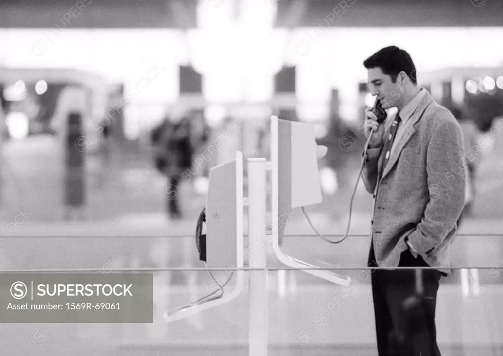 Businessman using pay phone in terminal, black and white