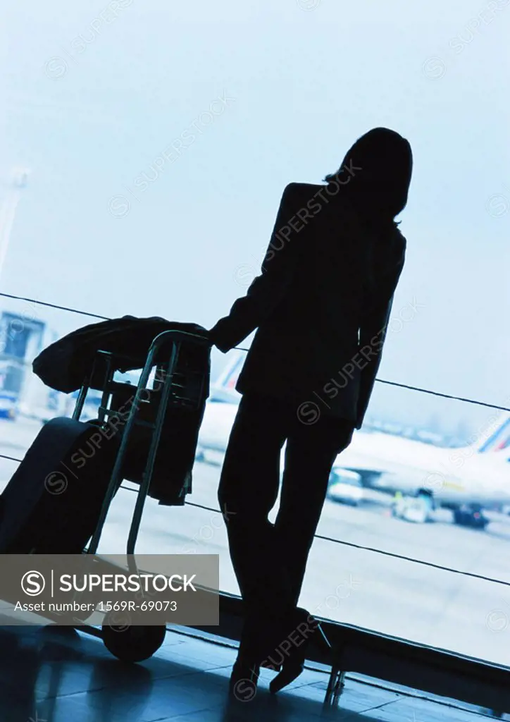Businesswoman standing next to luggage in airport, silhouette