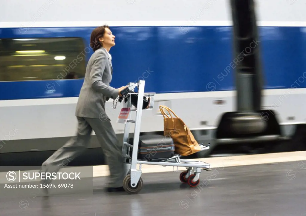 Businesswoman rushing on train platform with cart and luggage, next to train, blurred