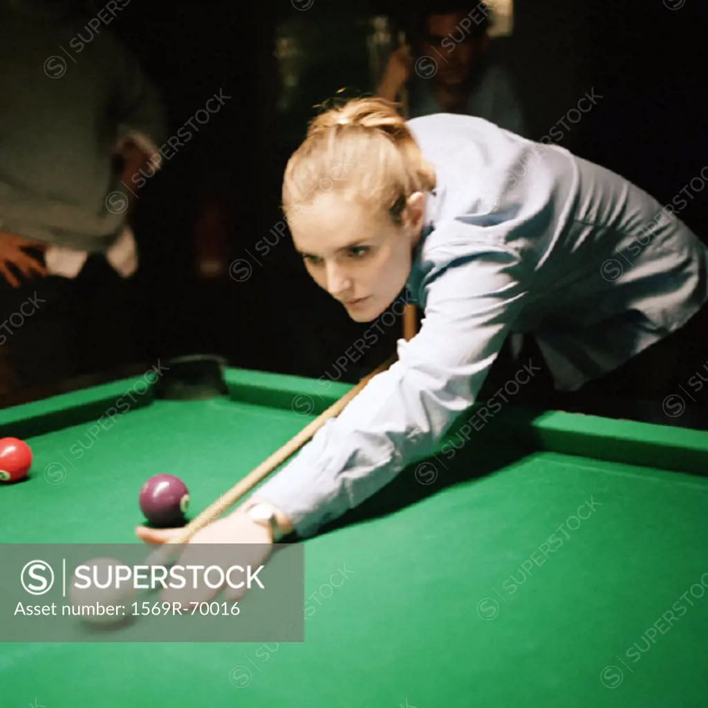 Young woman shooting pool, people standing in background