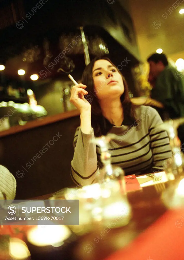 Young woman sitting in cafe, smoking a cigarette