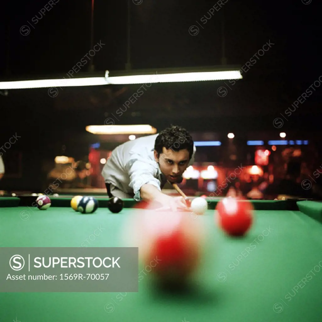 Young man shooting pool, billiard ball blurred in foreground