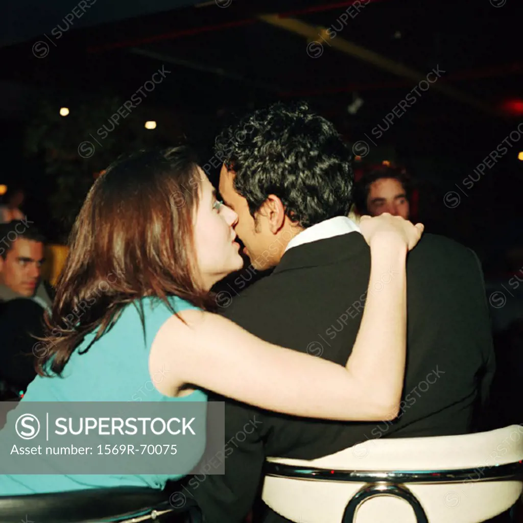 Young woman kissing young man on cheek in bar, rear view