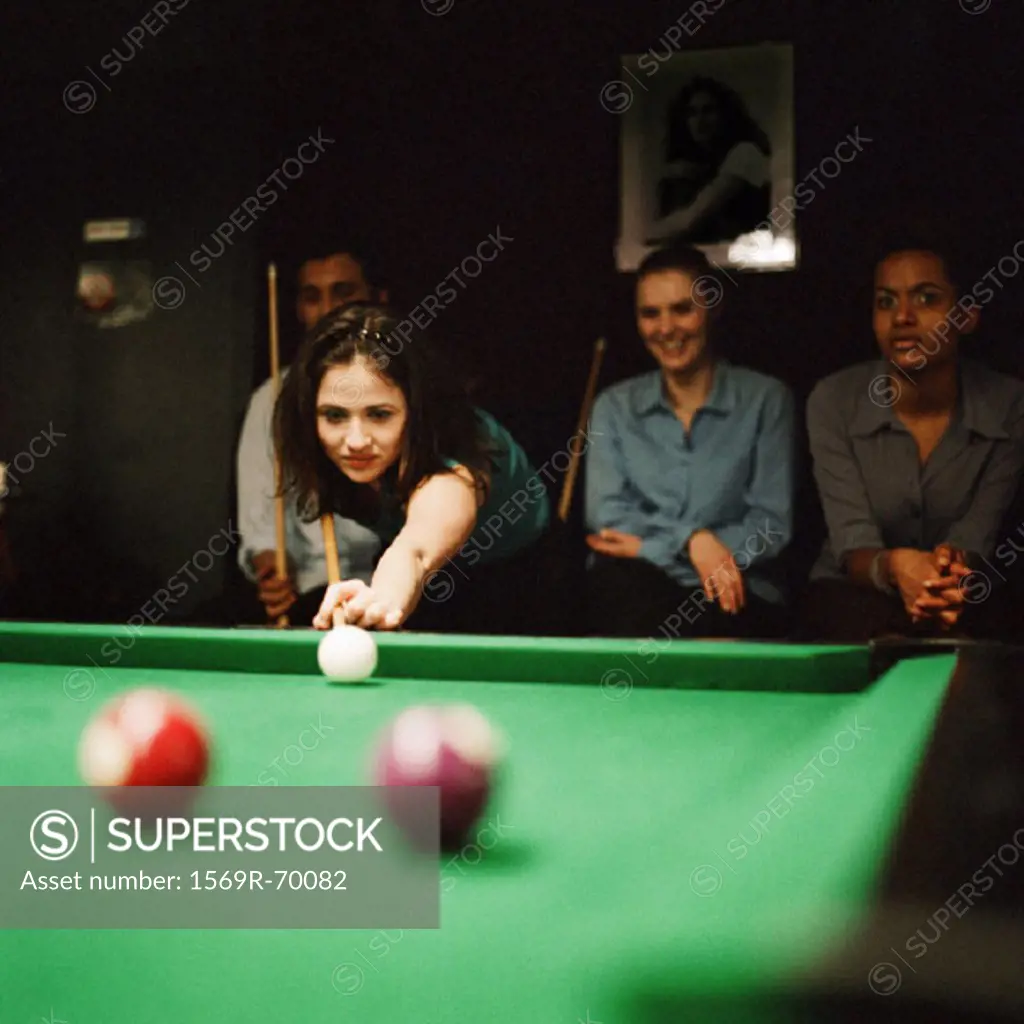 Young woman shooting pool, young people sitting in background