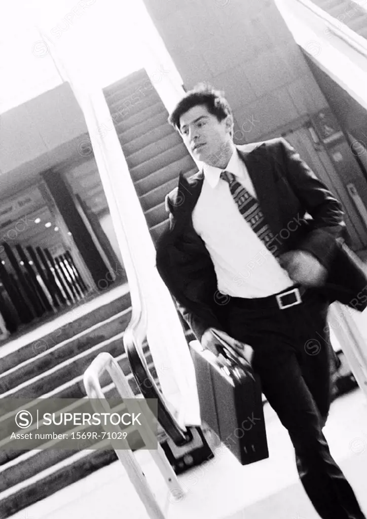 Businessman hurrying away from escalator, holding briefcase, blurred motion, b&w