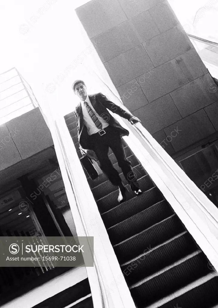 Businessman going down escalator, b&w