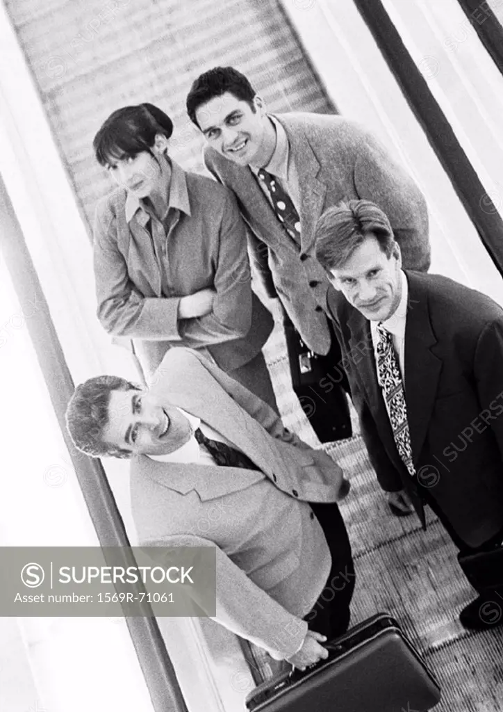Group of business people on moving walkway looking up at camera, high angle view, b&w