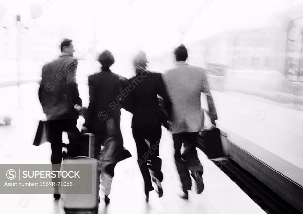 Group of business people hurrying on train platform, rear view, blurred, b&w