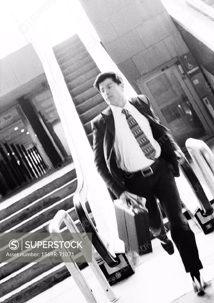 Businessman getting off escalator, running and holding briefcase, blurred, b&w