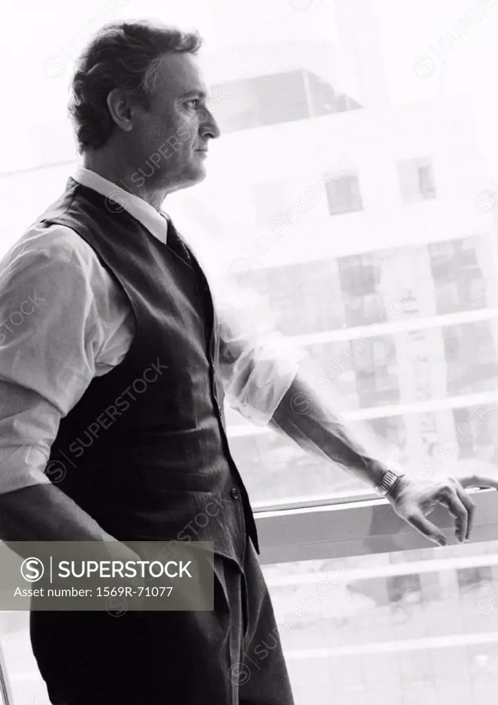 Businessman standing next to window looking out, side view, b&w