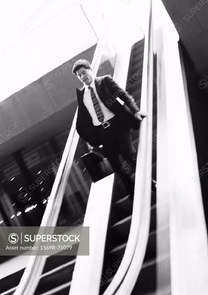 Businessman going down escalator, looking down, b&w
