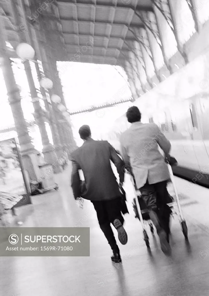 Businessmen hurrying on train platform, blurred, rear view