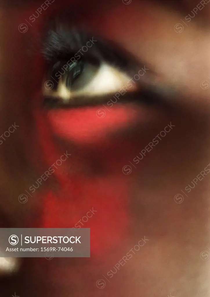 Woman´s eye looking up with red make-up on face, close-up, blurred