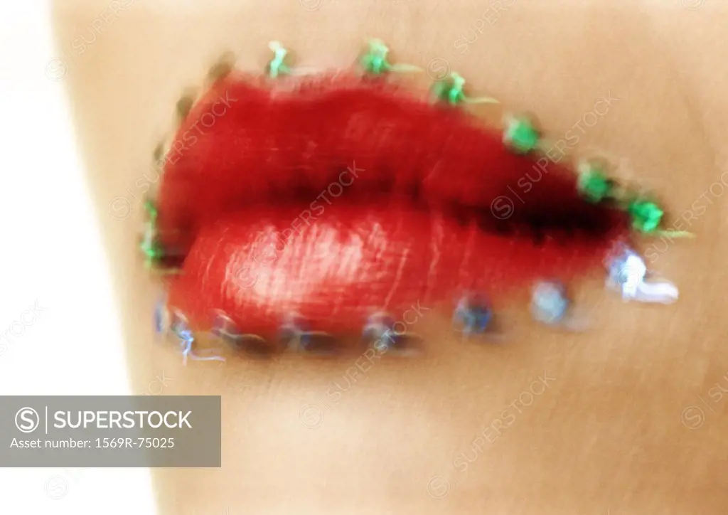 Woman wearing red lipstick, close up of mouth with jewel adornments, blurred