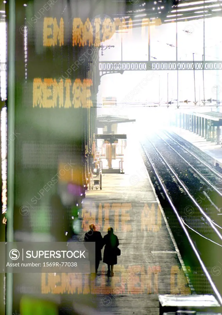 Couple walking on train platform, information sign superimposed