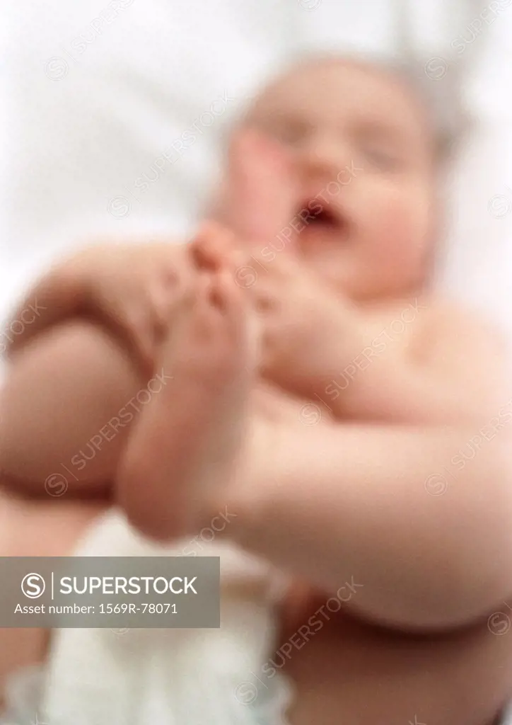 Baby lying on back, holding feet, blurred
