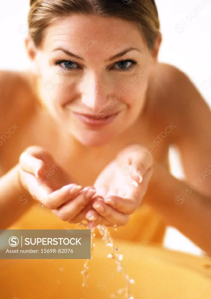 Woman cupping water in hands, smiling at camera, front view