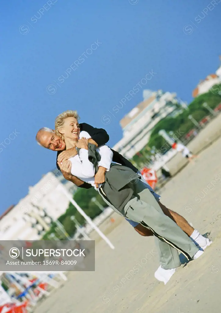 Mature man standing behind mature woman with arms around her on the beach
