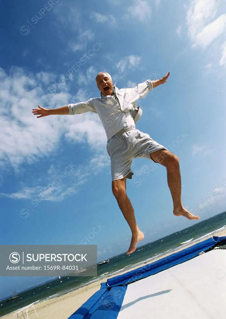 Mature man jumping on trampoline at the beach