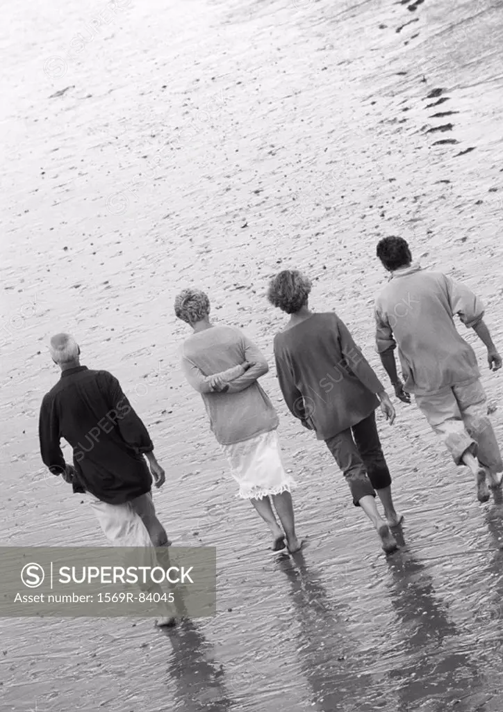 Four mature adults walking down the beach, view from rear, B&W