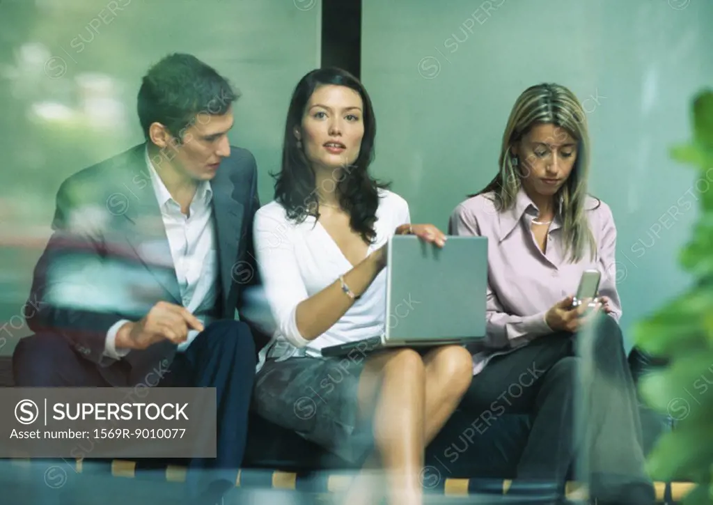 Businesswoman sitting between co-workers, looking up from laptop