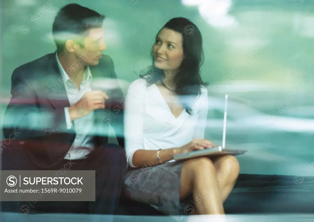 Businessman and businesswoman sitting together with laptop, looking at each other