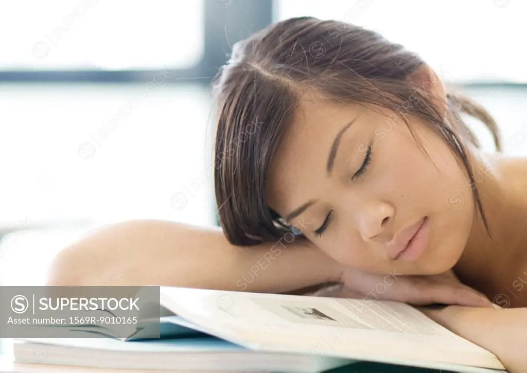 Young woman resting head on books, with eyes closed