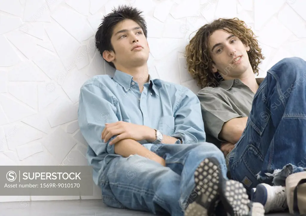 Two young men sitting on ground, leaning back against wall
