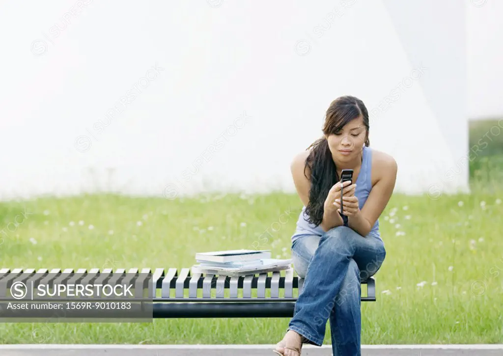 Young woman sitting on end of bench looking at cell phone