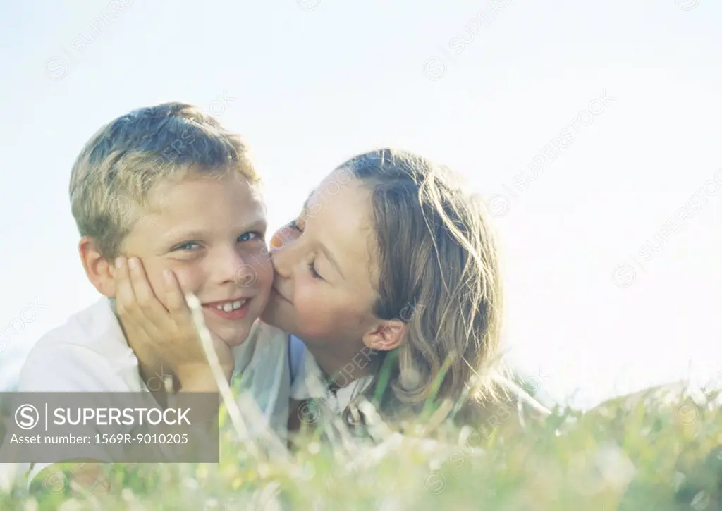 Boy and girl lying on grass, girl kissing boy on cheek