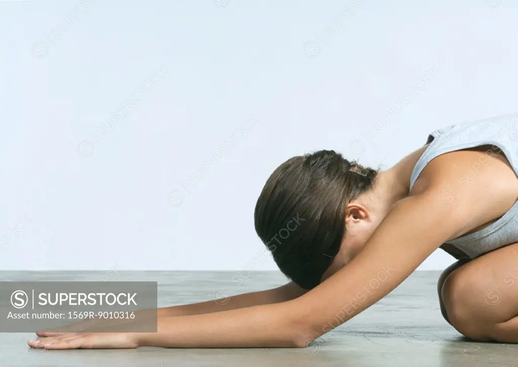Young woman kneeling on floor, stretching