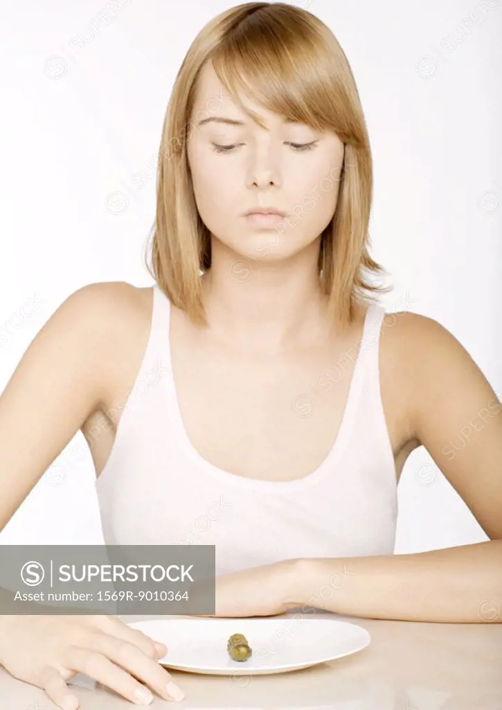 Young woman looking down at single pickle on plate