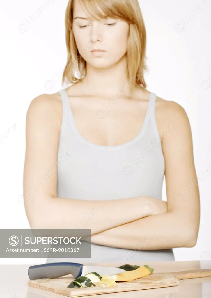 Young woman with arms folded looking down at sliced zucchini