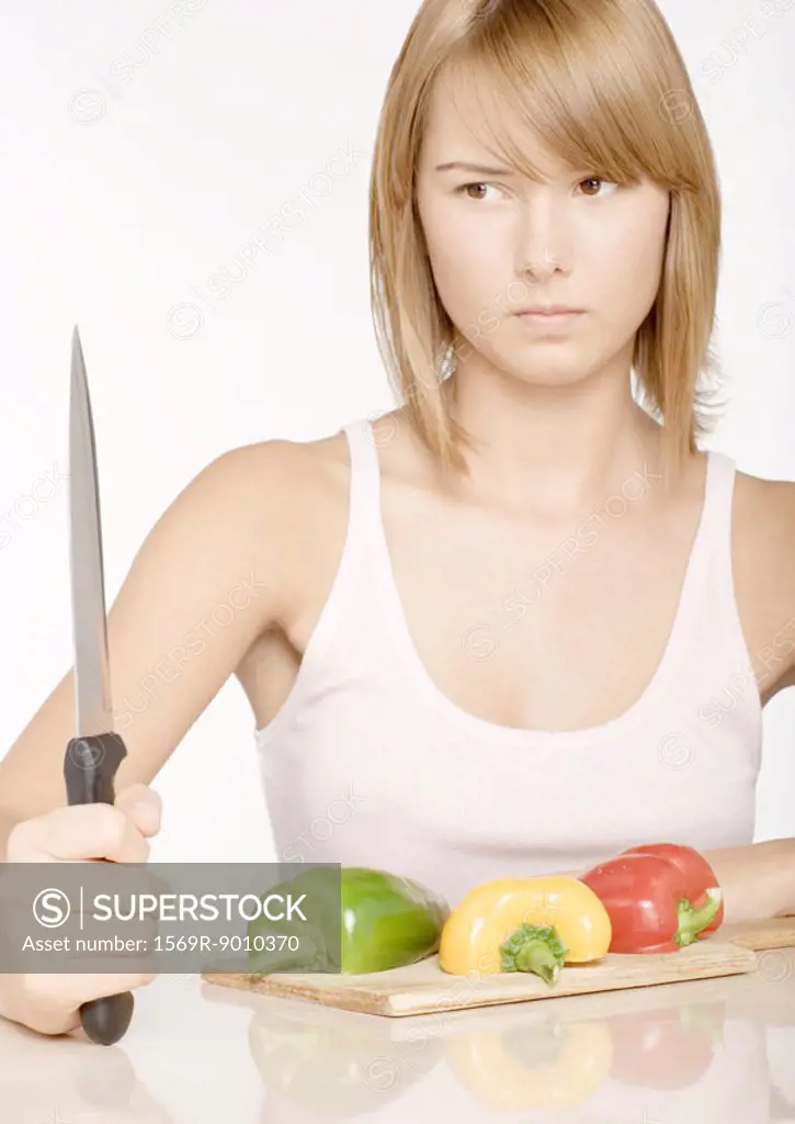 Young woman holding up knife in front of bell peppers