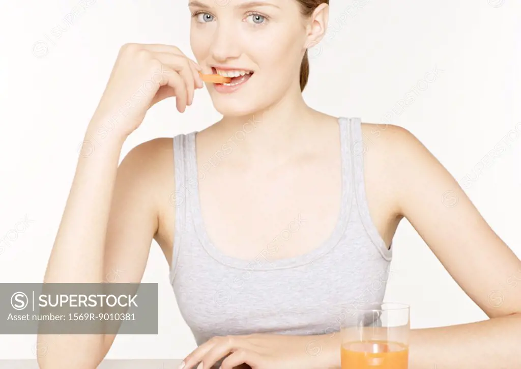 Young woman eating carrot stick and drinking carrot juice