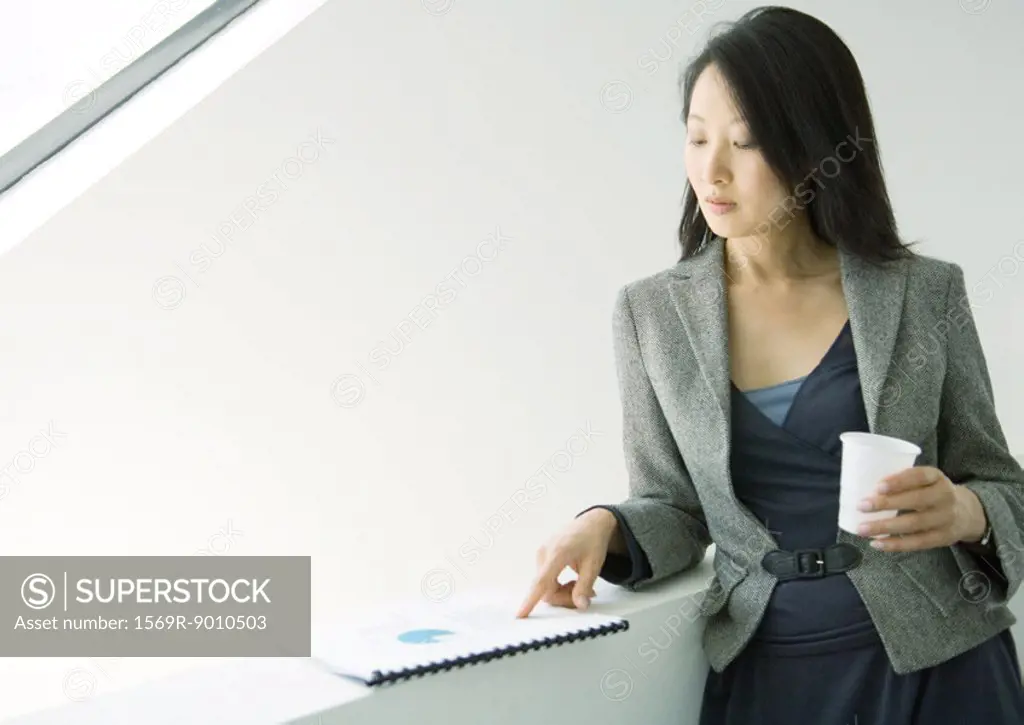 Businesswoman looking at report and holding cup